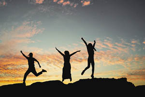 Three people jumping up with joy at sunset-Kirtan